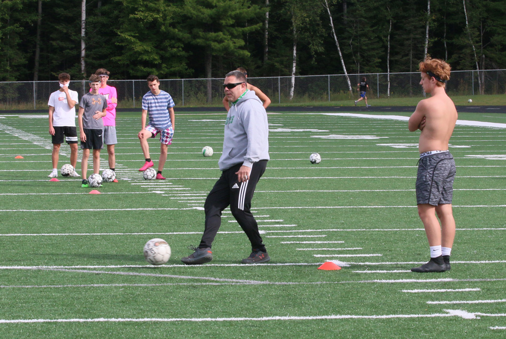 Head soccer coach Nathan Bates shows players how to pass the ball in a drill.